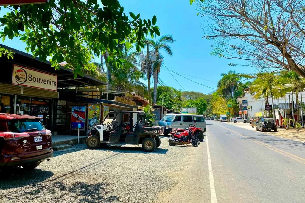 The main road through Playa Potrero, Costa Rica, with local shops, parked ATVs, and palm trees on a quiet afternoon