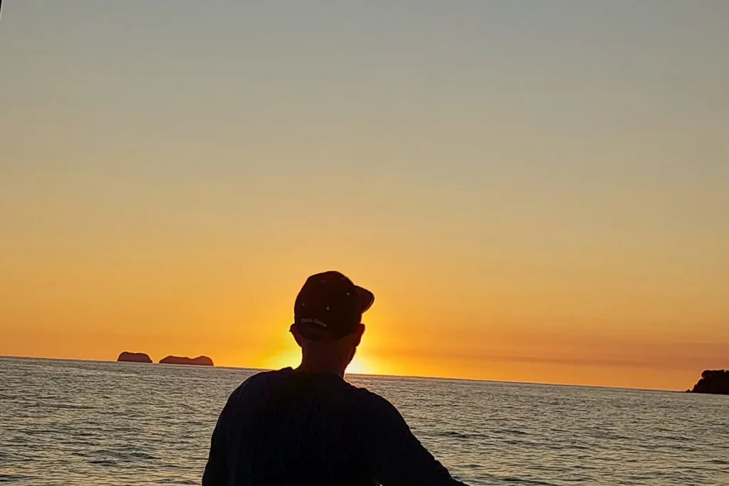 Silhouette of a person standing at the rail of a boat watching the golden sun set over the Pacific off Playa Potrero, Costa Rica