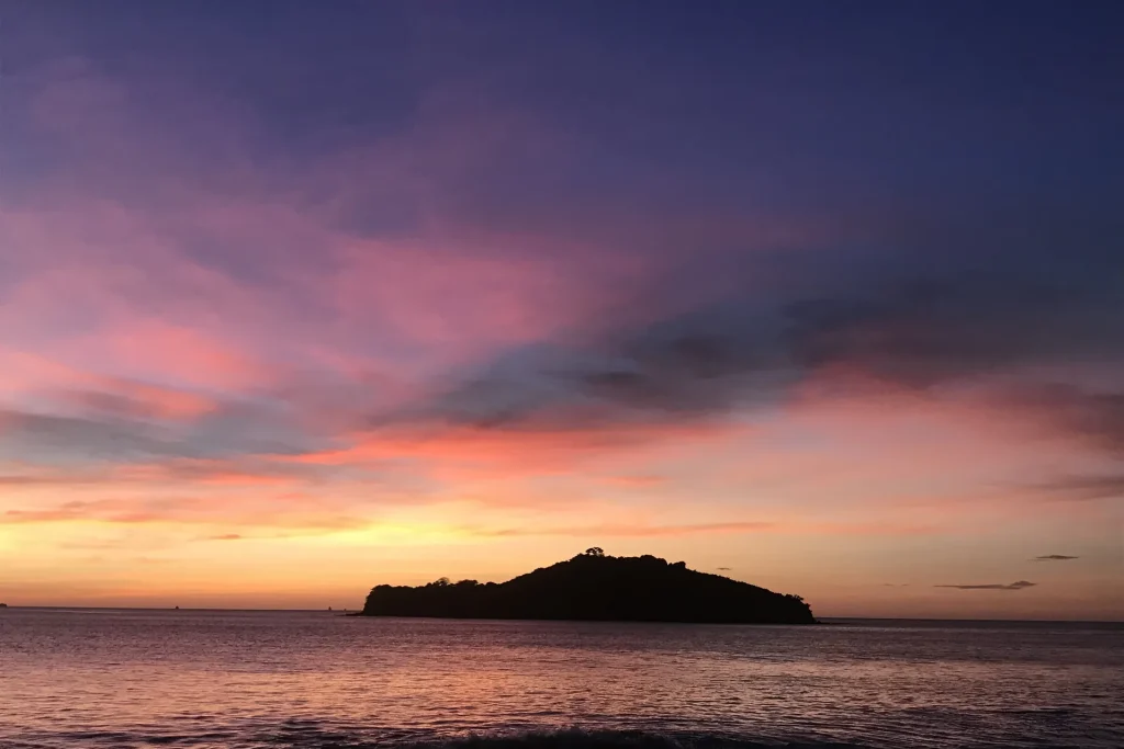 Purple and pink sunset sky over a single island silhouette at Playa Prieta, Playa Potrero, Costa Rica
