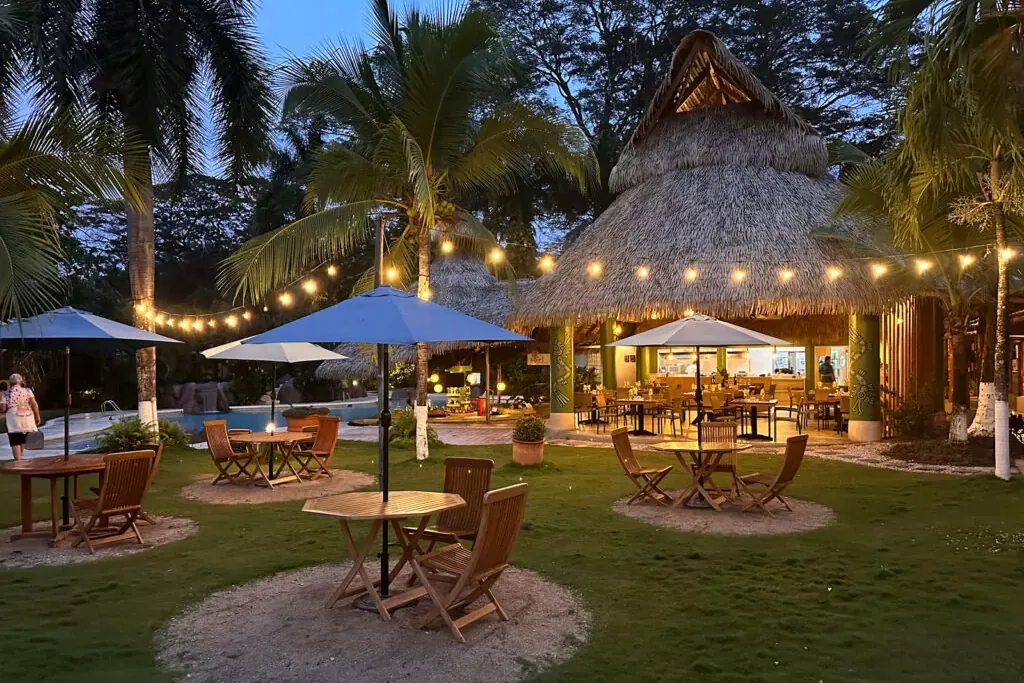 A thatched-roof poolside garden restaurant lit with string lights at dusk at a resort in Playa Potrero