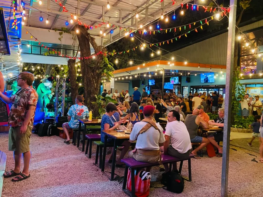 People of all ages enjoying live music and drinks under string lights at Potrero Brewing Co. on a night out in Playa Potrero