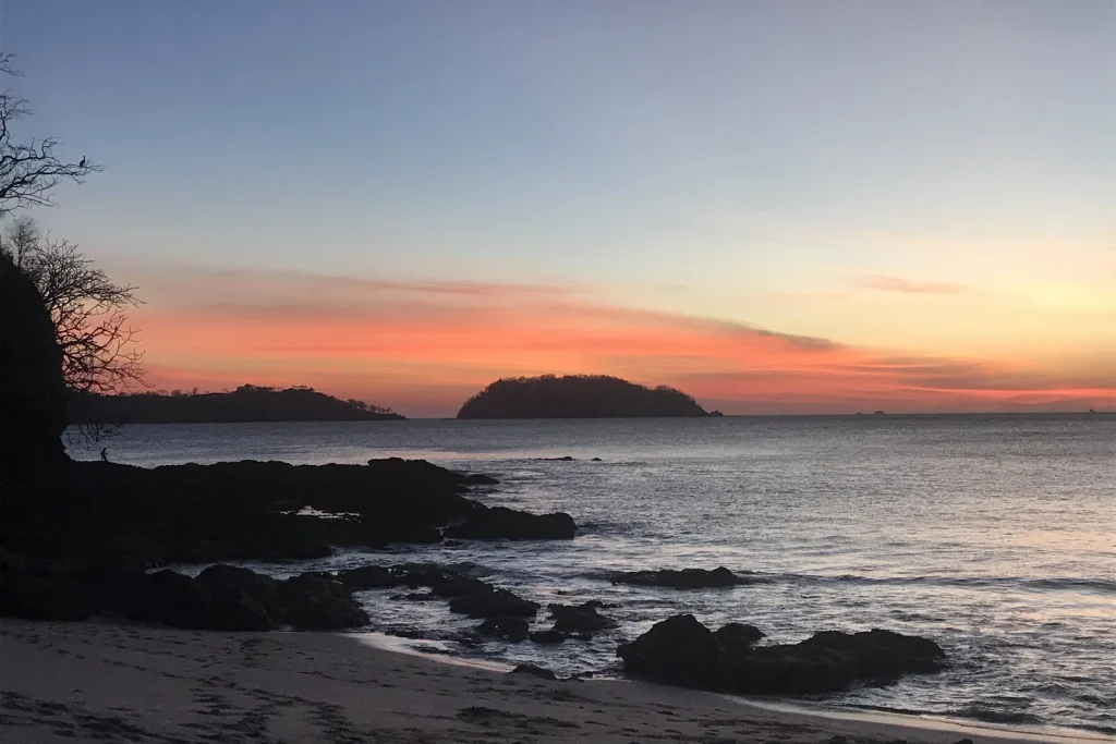 Coral and orange sunset behind the island at Playa Penca, with rocky tide pools in the foreground, Guanacaste, Costa Rica