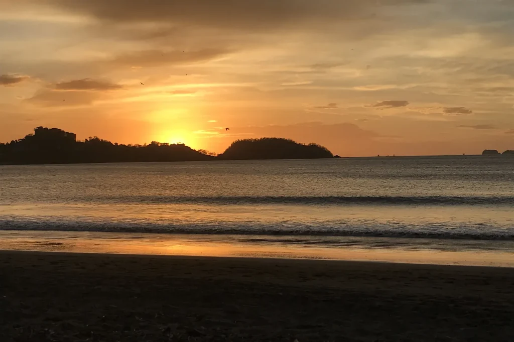 Golden sunset behind the headland with the sun reflecting on wet sand at Playa Potrero, Guanacaste, Costa Rica