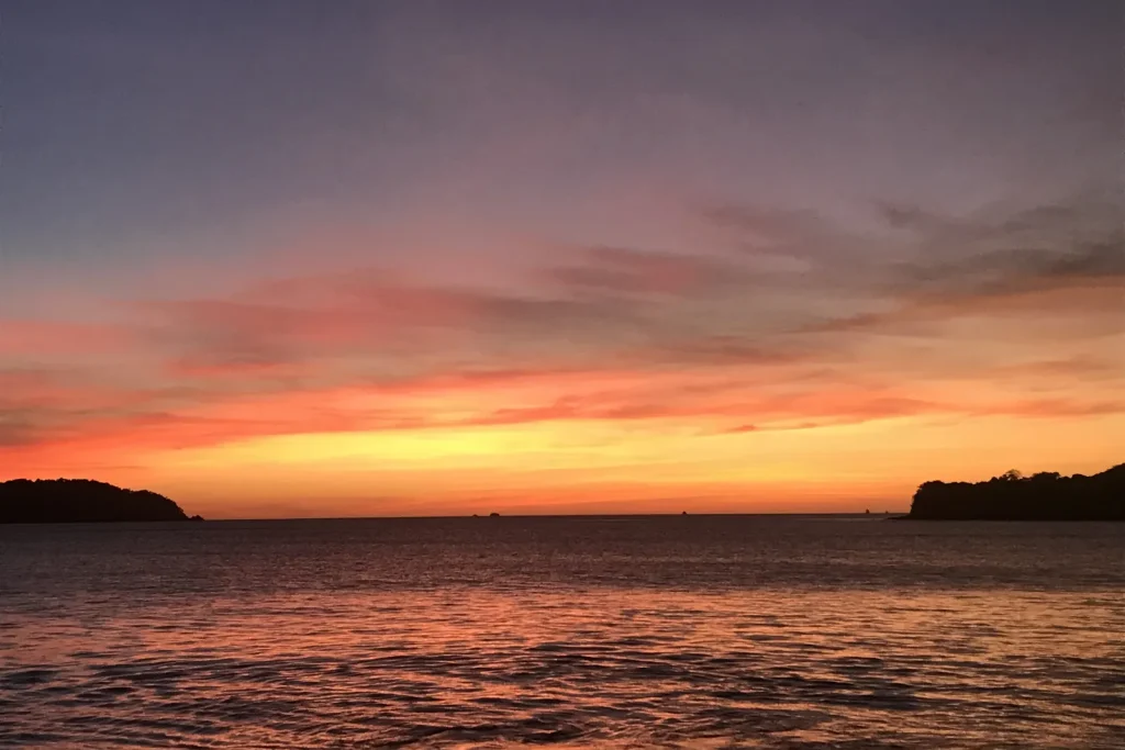 Fiery orange, red and purple sunset over the water between two headlands at Playa Prieta, Guanacaste, Costa Rica