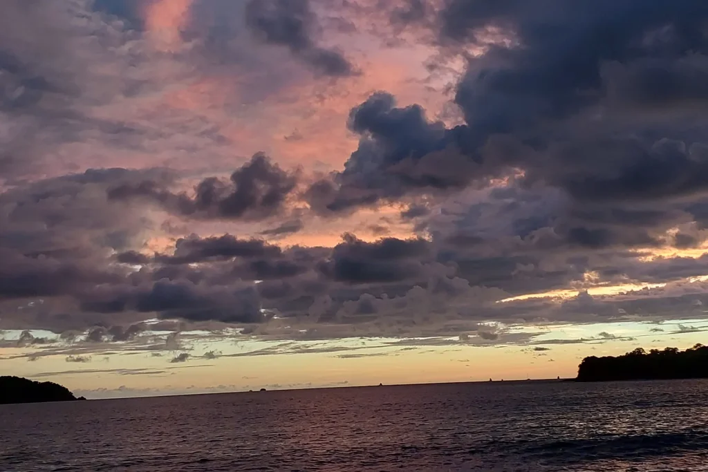Moody purple and pink storm clouds at sunset over the water near Playa Potrero — rare green-season color, Guanacaste, Costa Rica