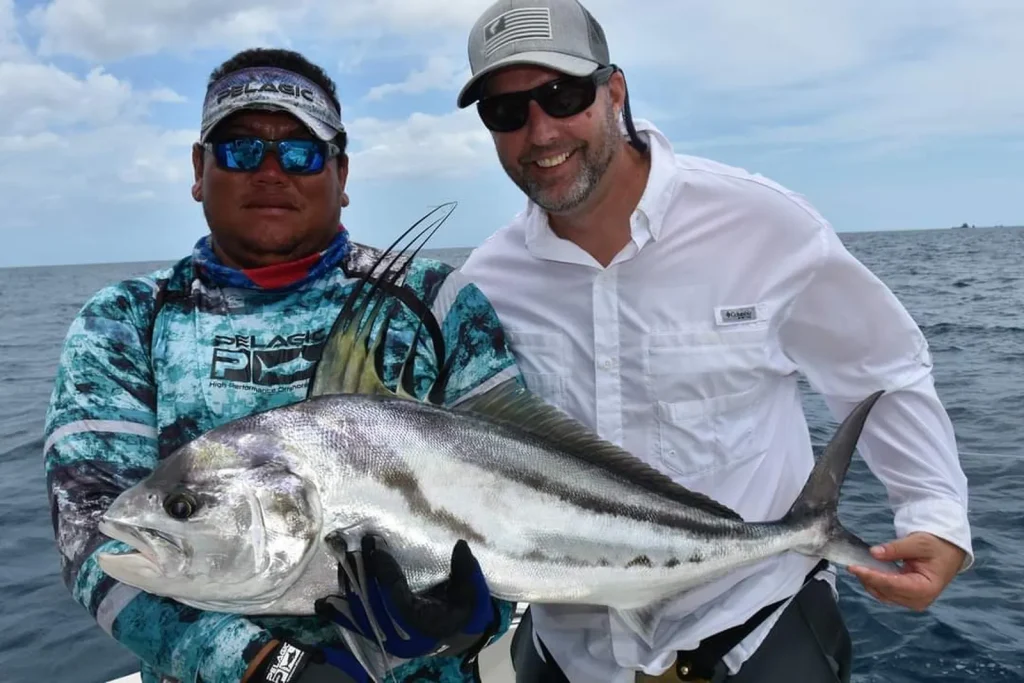 Angler and guide holding a roosterfish, its comb-like dorsal fin raised, on a calm-water inshore charter near Playa Potrero